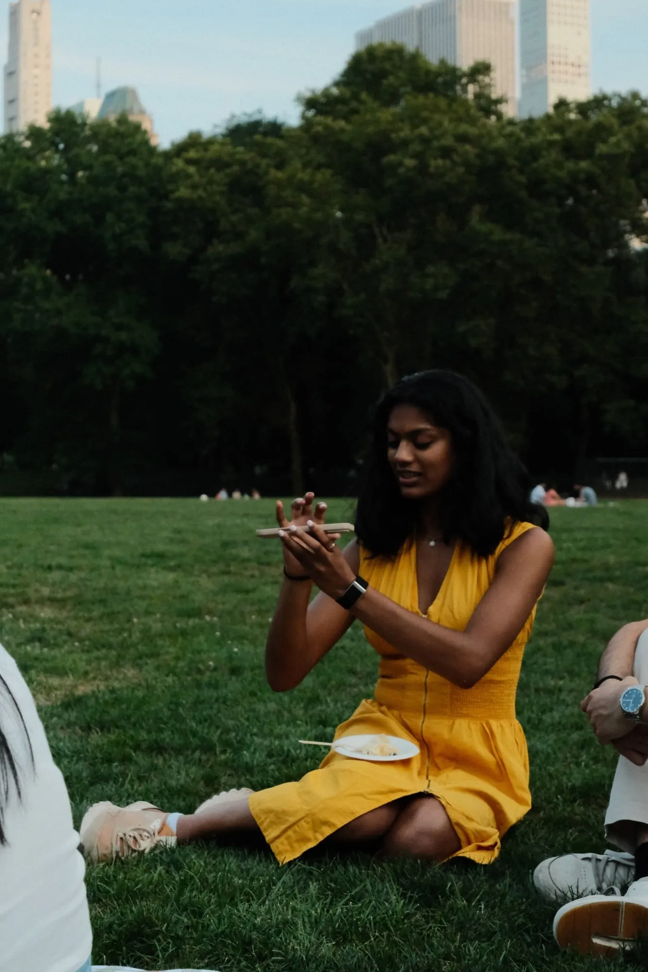 sahi in a yellow dress sitting on the grass in central park, reading spelling bee words off her phone